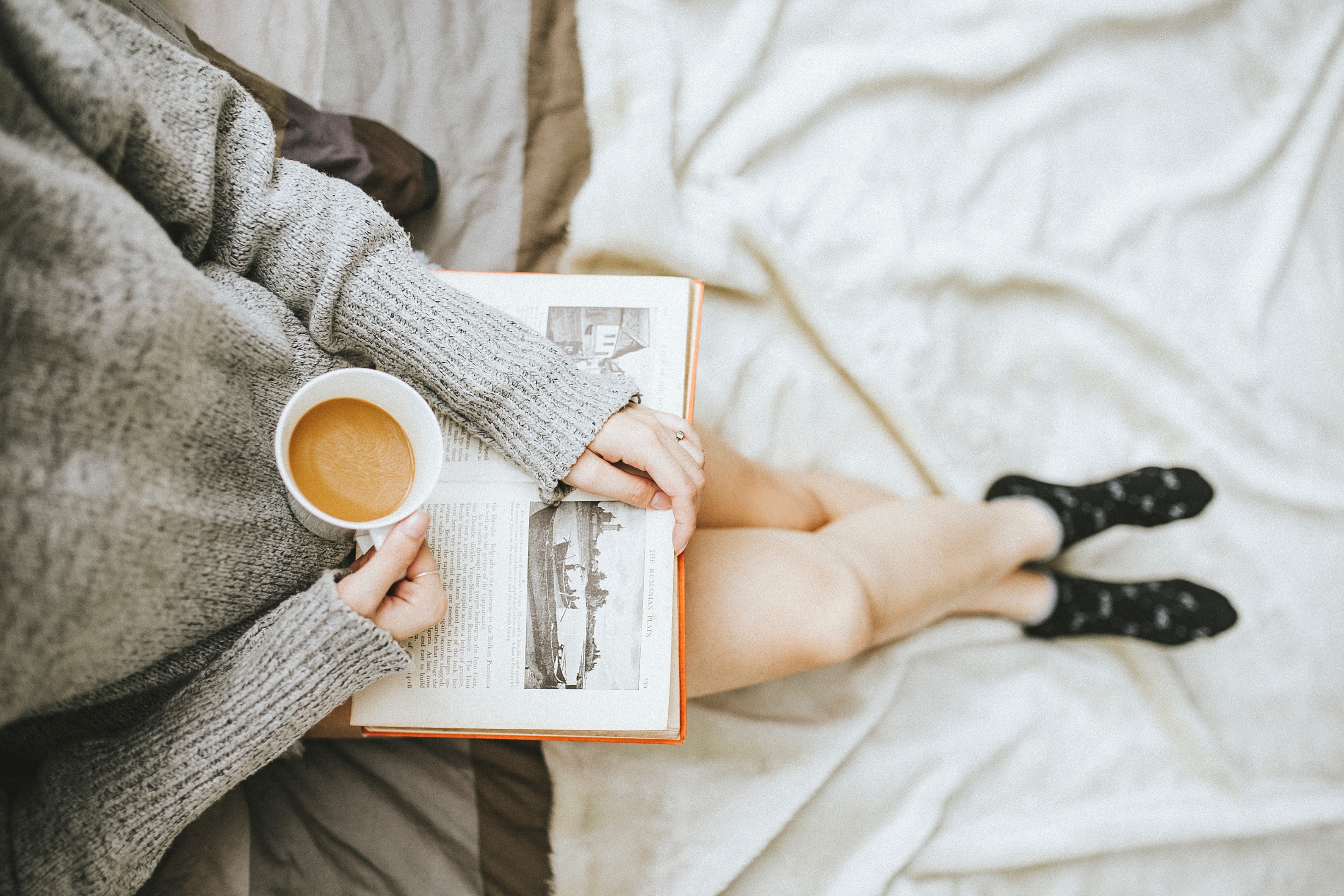 En person läser en bok och dricker kaffe