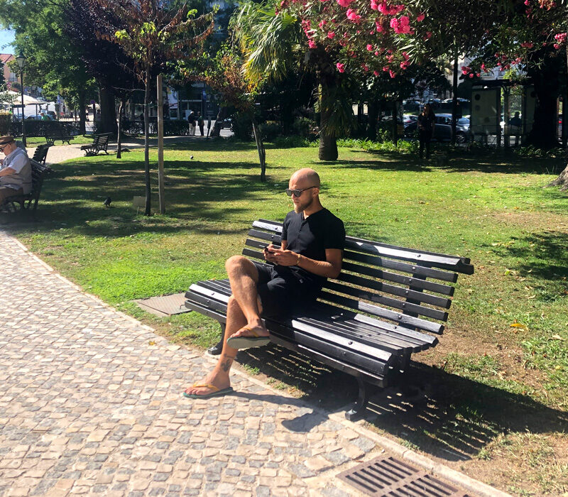 Christoffer på en parkbänk med sin mobil i Jardim braancamp