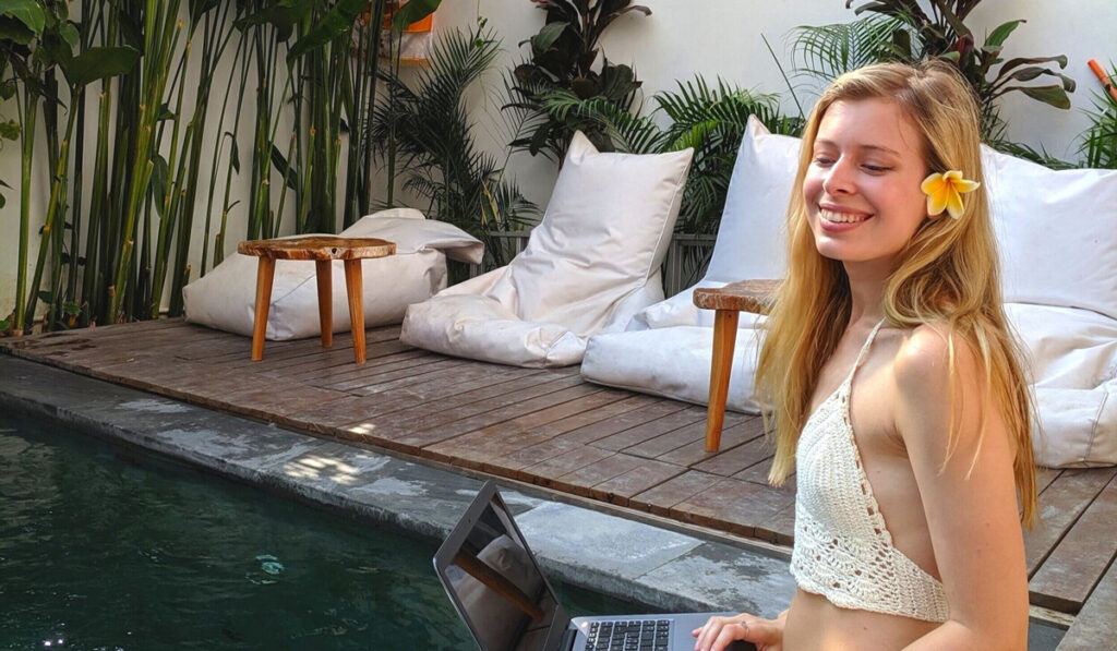 Julia Lundin sitter med sin laptop vid poolen och ler