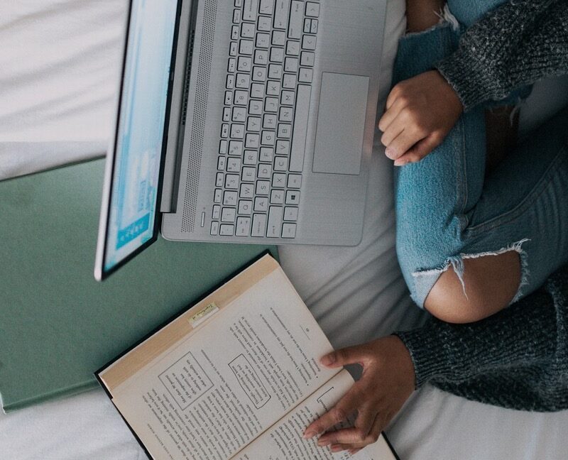 girl sitting on bed with laptop and books studying