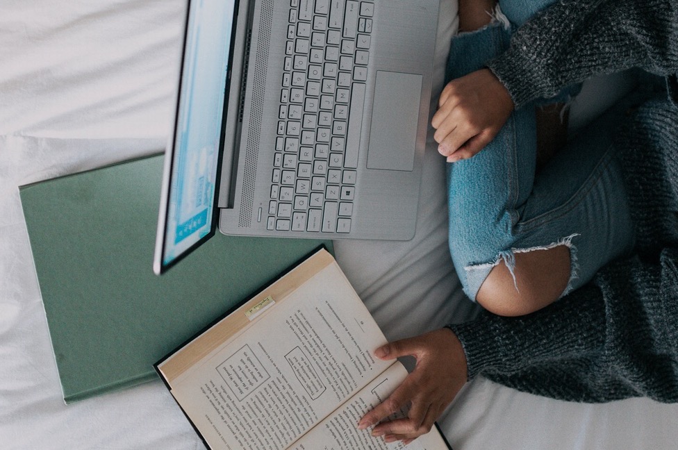 girl sitting on bed with laptop and books studying